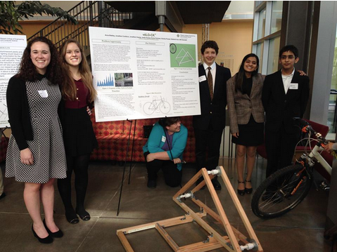 (from left) Juniors Anna Blakely, Emma Perlman, freshman Jonathan Cordisco, junior Ruhika Prasad, and sophomore Siddharth Suri stand in front of their presentation board and prototype while adviser Meg Kilmer crouches under the board.