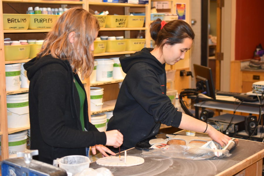 Evie Babbie (left), vice president of National Art Honors Society and Sage Taylor (right), president, gets their hands dirty with clay as they work on their projects in the ceramics room.