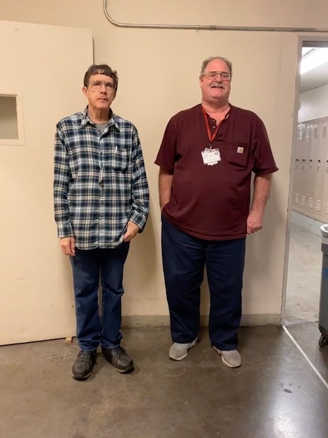 Carl Miller (left) stands with Rodger Hastings (right) next to the janitorial breakroom.